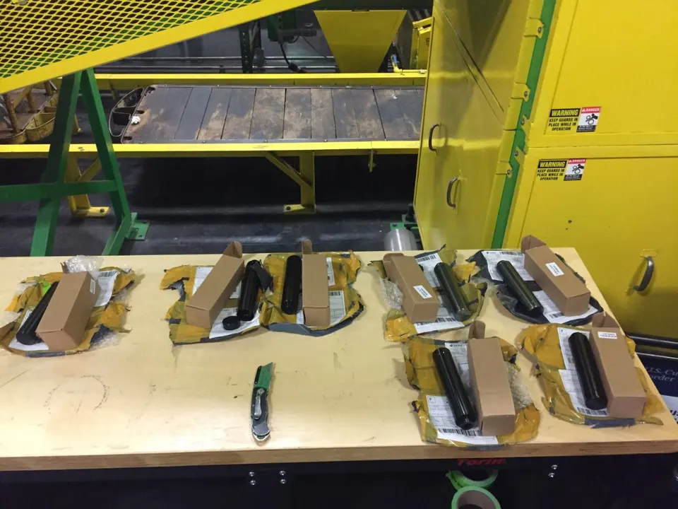 Several cardboard-boxed parcels with black cylindrical items wrapped in yellow padding lie on a wooden table in an industrial facility.