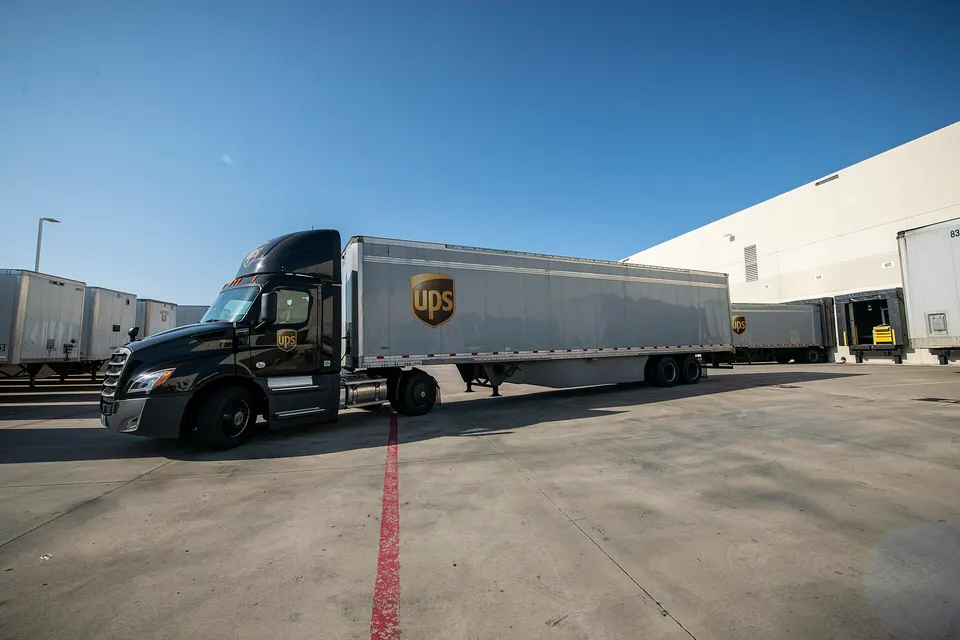 A UPS semi-trailer truck backing up to an offload dock at a facility in Arlington, Texas